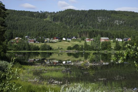 typical red and white houses in norway with reflection in the water of the leira fjord in middle norway