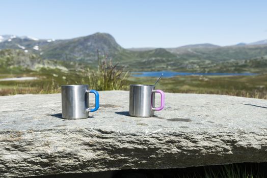 time for relax when travel around norway with two metal coffee cups on a rock and then nature mountains as background