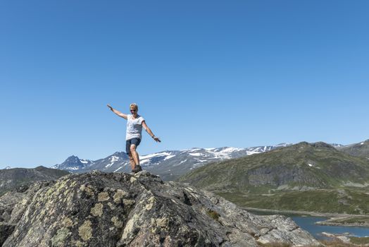 adult woman happy standing on a rock looking over the national park from bitihorn to stavtjedtet with lakes fjord and snow on the mountains