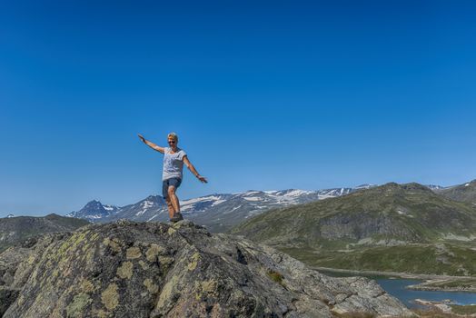 adult woman happy standing on a rock looking over the national park from bitihorn to stavtjedtet with lakes fjord and snow on the mountains