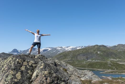 adult woman happy standing on a rock looking over the national park from bitihorn to stavtjedtet with lakes fjord and snow on the mountains