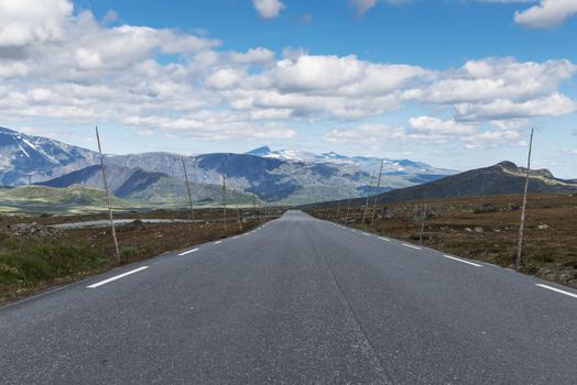 empty nroad in norway with Poles for the snow blades and mountains with snwo as background in July on the valdresfya nature area