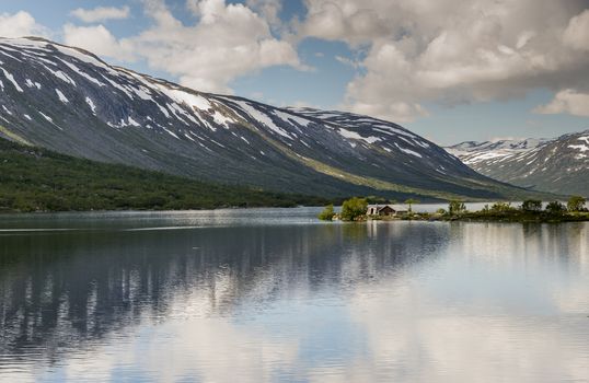 old house at a fjord with mountains with snow in the summer as background