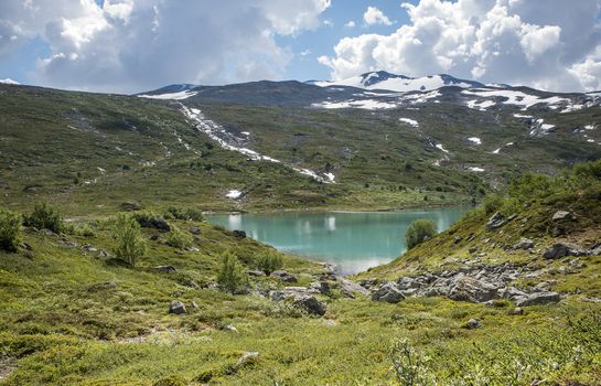 small lake in nature norway near gamle strynefjellsveg with blue water and mountains with snow in background