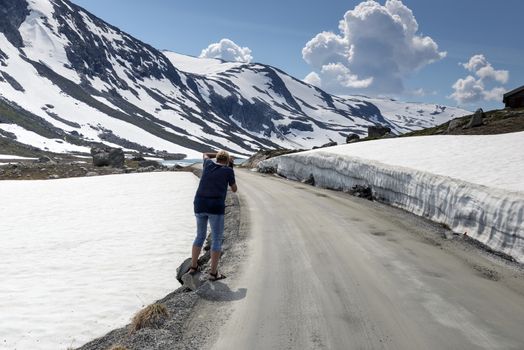 woman making photo of the snow on the gamle strynefjellsvegen road,  one of the most beautifull auto roads in norway with snow in summer 