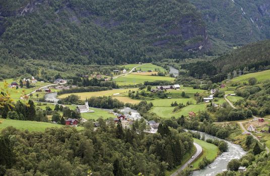 a village in norway with some houses and a church in the mountains near the river