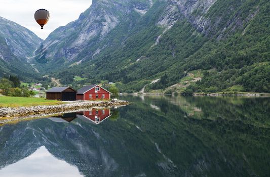 typical norway fjord with red wooden houses and reflection in the water and hot air balloon in the sky