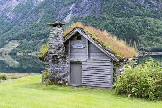 old fairytale-like house of wood with chimney of stacked slate and a roof with planting and trees on a fjord in Norway with garden with red flowers and green plants near Balestrand
