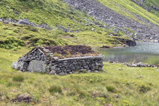 very old hut house build from stacked stones an plants on the roof at a fjord in norway at the gaularfjellet road