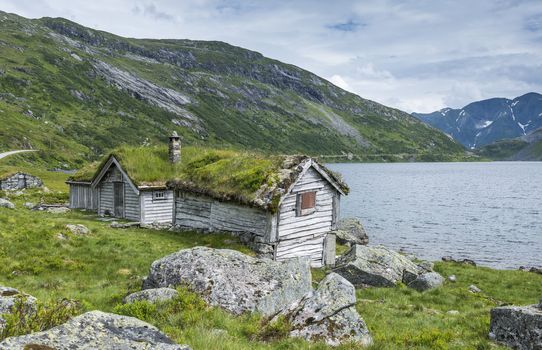 old fairytale-like house of wood with chimney of stacked slate and a roof with planting and trees on a fjord in Norway with garden with red flowers and green plants near Balastrand
