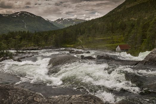 raw waterfall with small house and mountains with snow as background near Balestrand