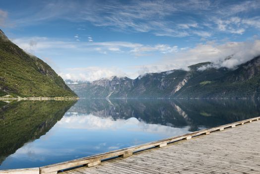 reflection of mountains in fjord in norway with wooden walking track in front