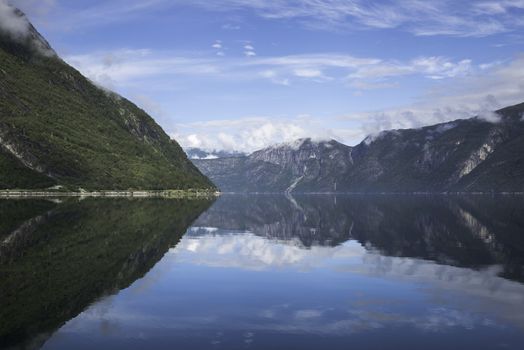 reflection of the mountains in the geirangerfjord in norway with blue water and sky