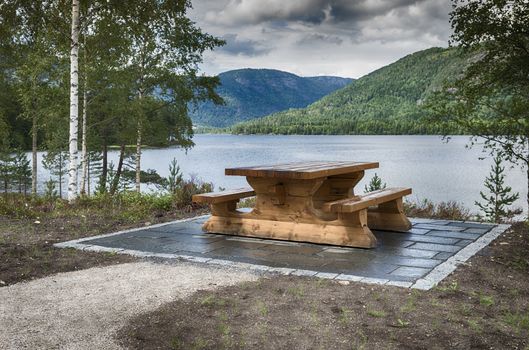  wooden bench at fjord in norway with the mountains and green forest as background