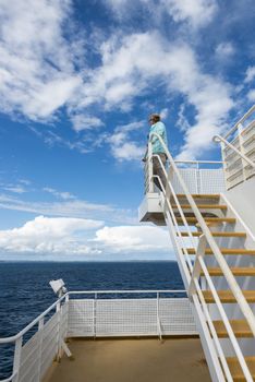 adult woman in blue sweater on ferry from Norway to Sweden with blue sky and white clouds and the caost of sweden as background