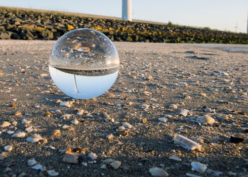 crystal spehere with reflection of windturbine and shell on the beach near windmill park