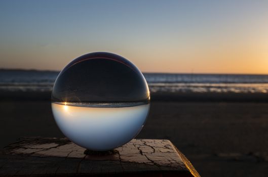 sunset on the beach on wooden pole captured in glass crystal sphere