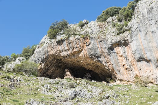 rocks with old ancient caves where people used to live and blue sky in andalusia with green grass landscape