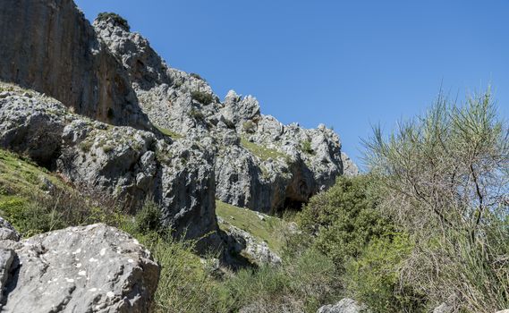 rocks with old ancient caves where people used to live and blue sky in andalusia with green grass landscape