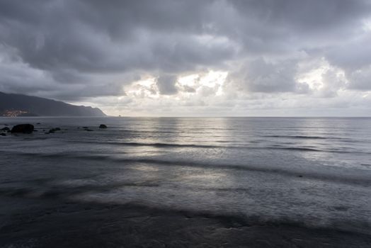 dark clouds in the evening over Madeira island with clouds and rocks and lightened village in background