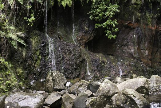 waterfall on madeira island on levada das 25 fontes tracking in wild nature with red rocks and stones