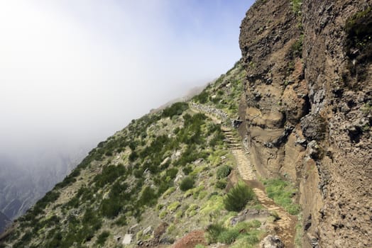 the high mountains at madeira island called pico arieiro with green plants and clouds on the left , the top is 1818 meters above sea level