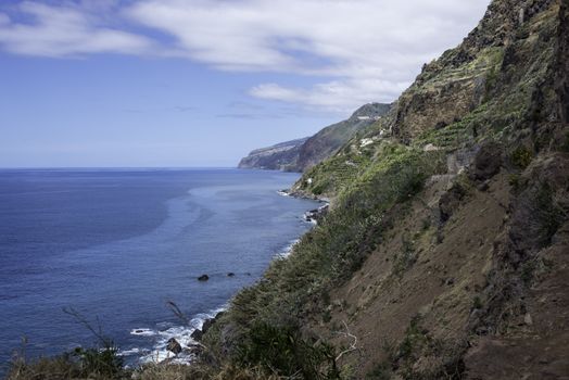 the volcanic rocks of the east caost of madeira island with blue sky and green vegetation near calheta village