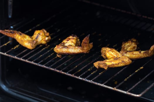 Roasted chicken wings on grill in the oven. Fresh grilled chicken meat. Dark background, shallow depth of field.