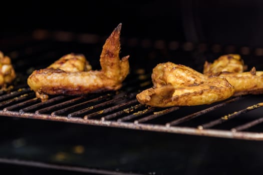 Grilled chicken wings on a metal grill. Fresh grilled chicken meat. Dark background, shallow depth of field.