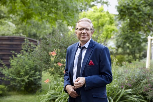 Portrait of middle-aged smiling man wearing blue jacket in the garden. Natural sunlight.