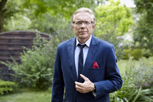 Portrait of middle-aged man wearing blue jacket in the garden. Natural sunlight.