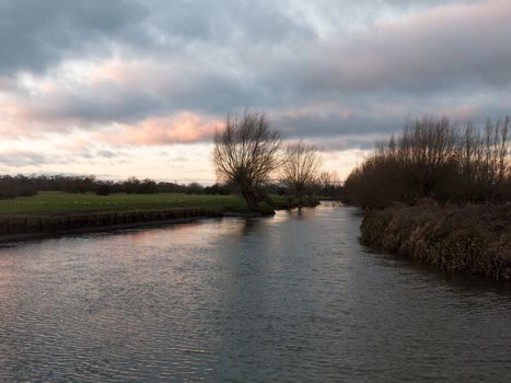 sunset moody sky winter autumn over green field with trees water; essex; england; uk