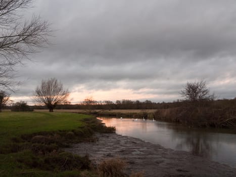 sunset moody sky winter autumn over green field with trees water; essex; england; uk