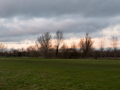 sunset moody sky winter autumn over green field with trees water; essex; england; uk