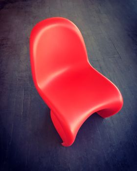 Red plastic chair on dark wooden floor. Modern design.