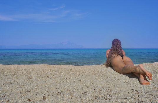 Girl with beautiful body with bikini is lying on the beach looking at sea.