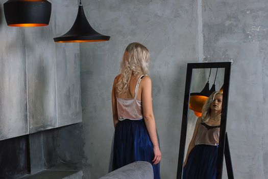 Young beautiful woman in cocktail dress standing near mirror