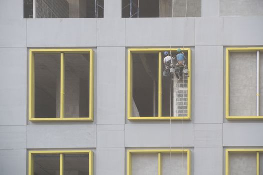 Construction worker abseiling plastering two people