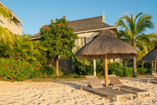 Beach at Mauritius island with wooden parasol,garden and bungalow, sunny day.