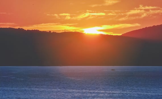 spectacular sunset behind a mountain overlooking the blue sea