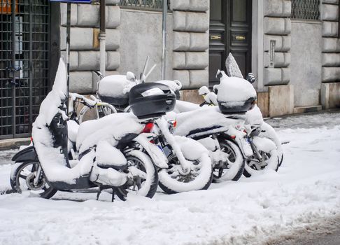 a group of snow-covered scooters in a city street