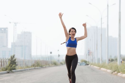 fitness, sport, victory, success and healthy lifestyle concept - happy woman winning race and coming first to finish red ribbon over group of sportsmen running marathon with badge numbers outdoors