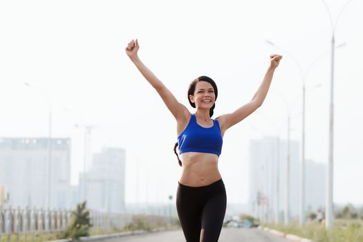 fitness, sport, victory, success and healthy lifestyle concept - happy woman winning race and coming first to finish red ribbon over group of sportsmen running marathon with badge numbers outdoors