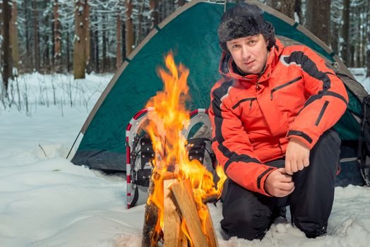 active tourist near the campfire in the tent camp in the winter forest