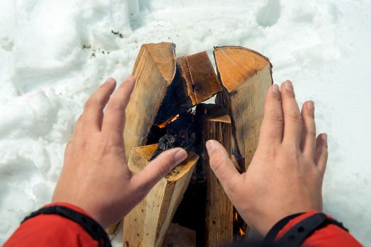 close-up photo - tourist warms his hands near the fire in the winter forest