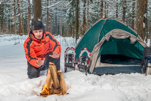 a frozen lost tourist near a tent warms his hands by the fire