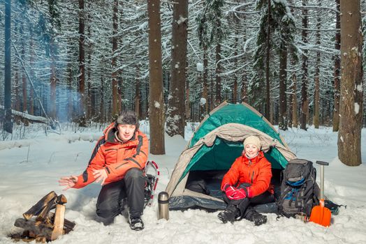 tourists in the winter forest - a man is warming his hands by the fire