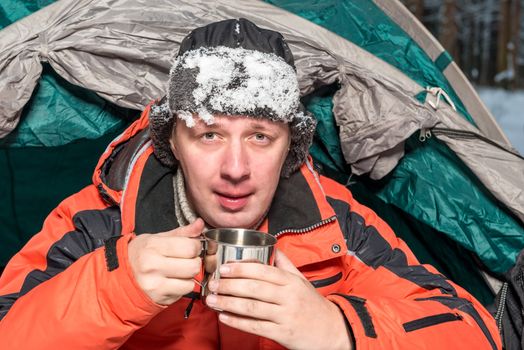 portrait of a frozen man with snow on a hat with hot tea in a camping