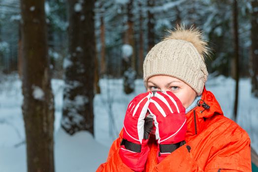 woman in winter clothes warmed in the winter forest with hot tea in a mug