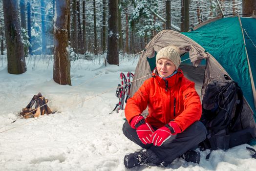 pensive tourist woman sits near a tent in a winter forest